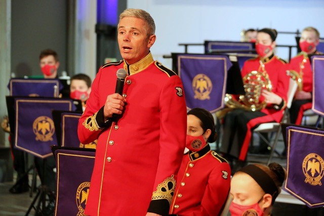 Man standing with a microphone in front of the youth band